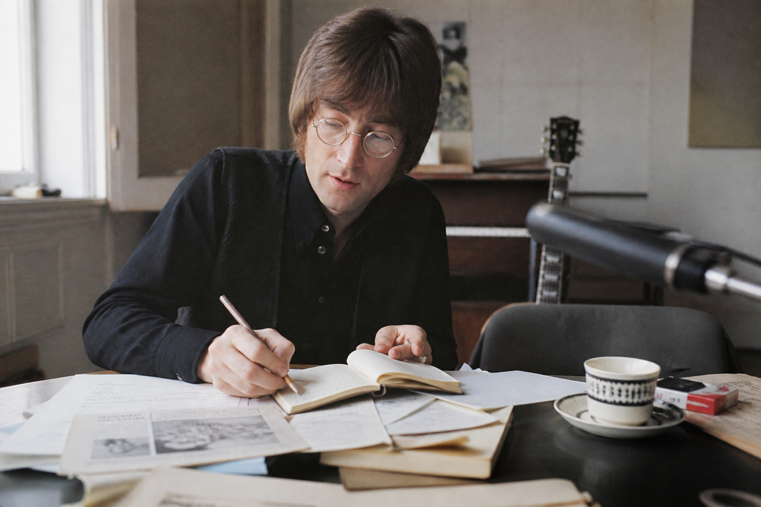 John Lennon writing lyrics in a notebook while reflecting on the world around him