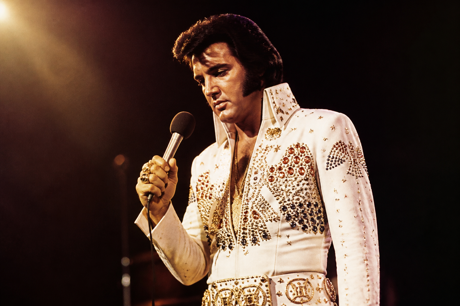 Elvis Presley-style stage performer holding a microphone under warm lights