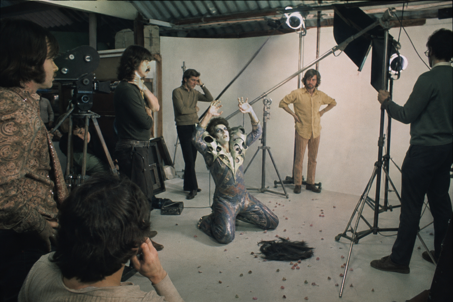 Vintage film crew watching a surreal performance unfold on a small promotional set