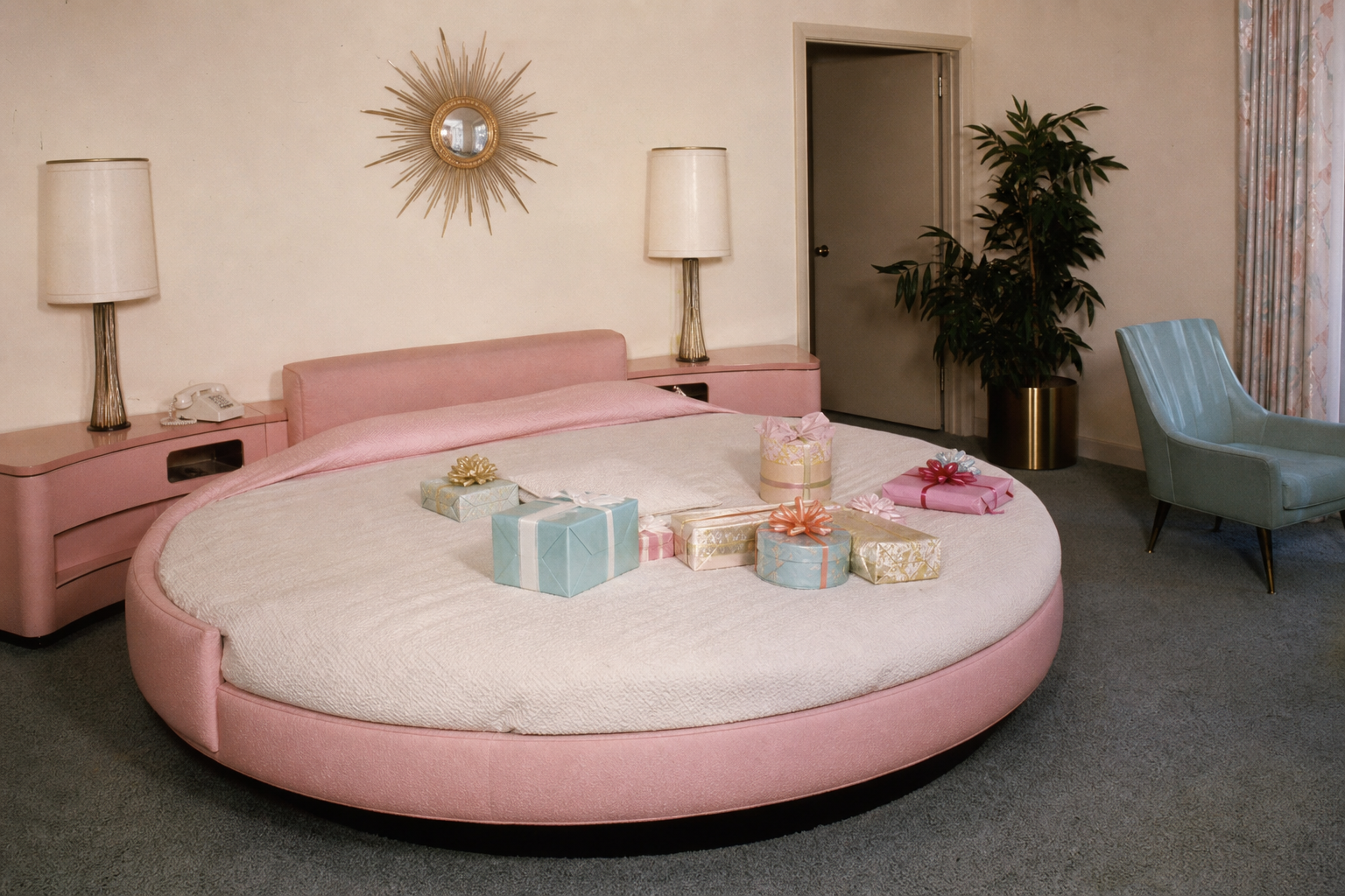 a round pink bed in a stylish 1960s bedroom, gift boxes on the covers